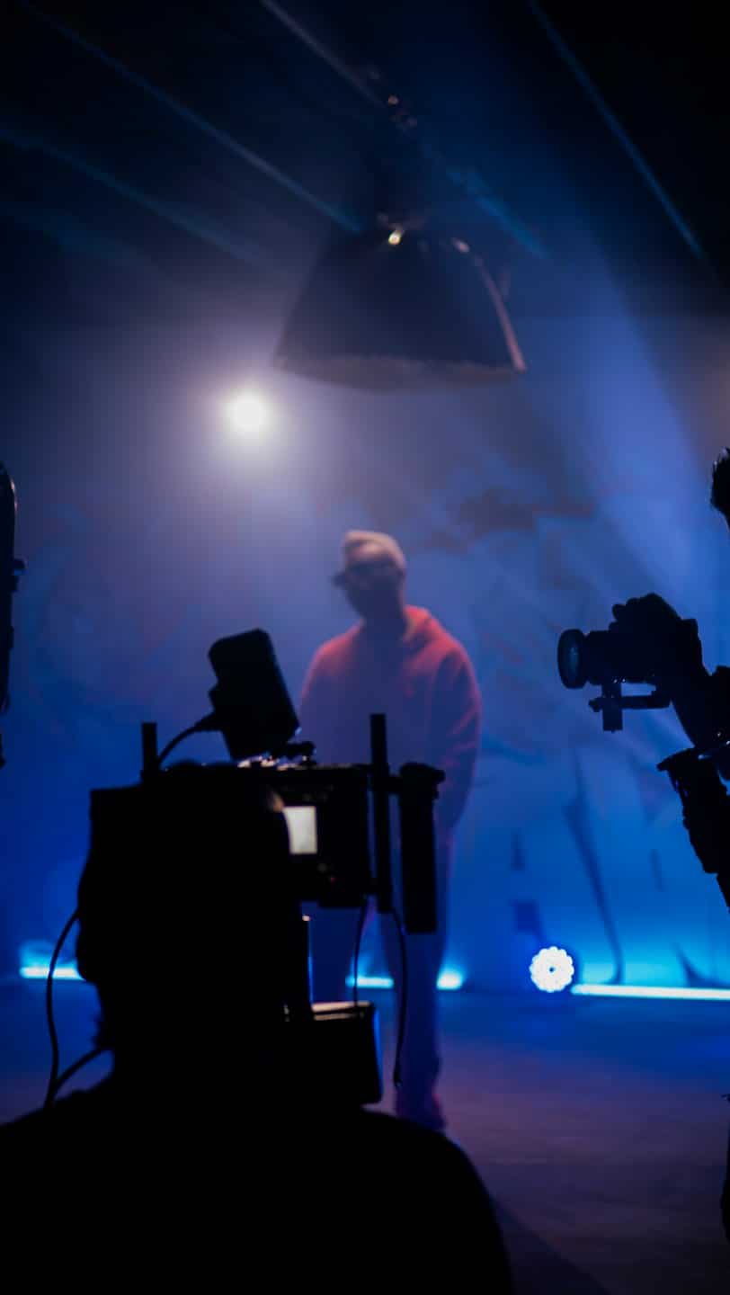 Film crew captures a person in a red hoodie on stage.