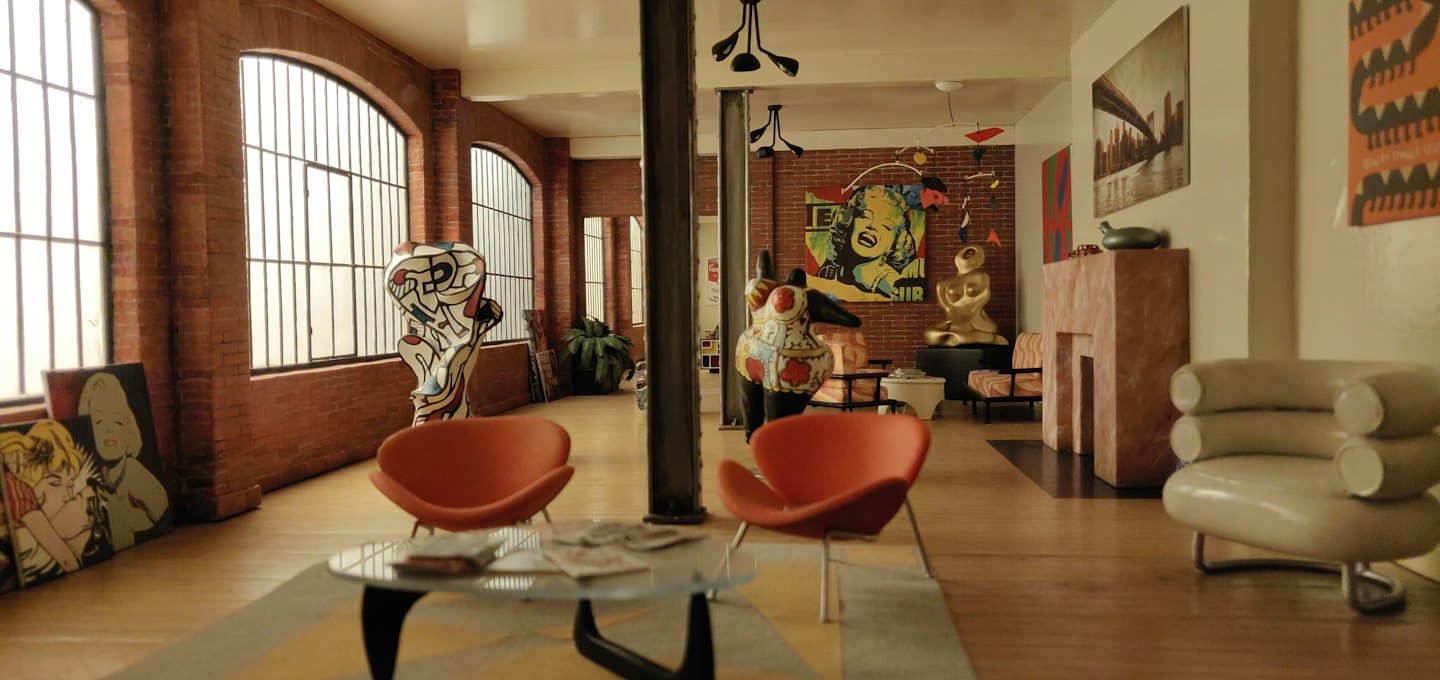 Modern loft apartment with art, orange chairs, and glass table.
