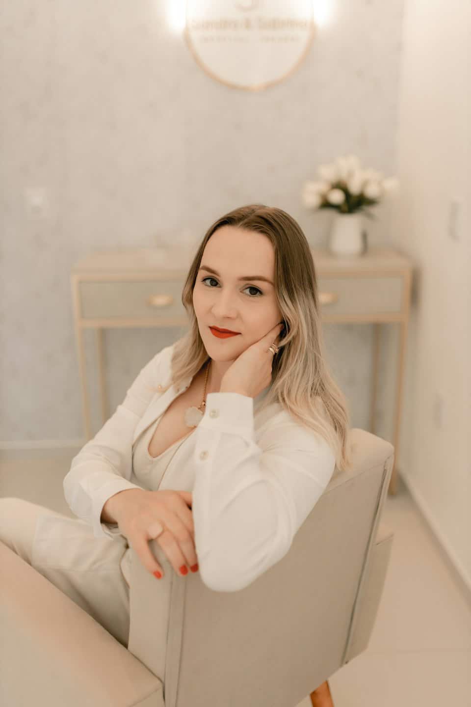Woman in a suit sitting in an armchair with her hand resting on her cheek.