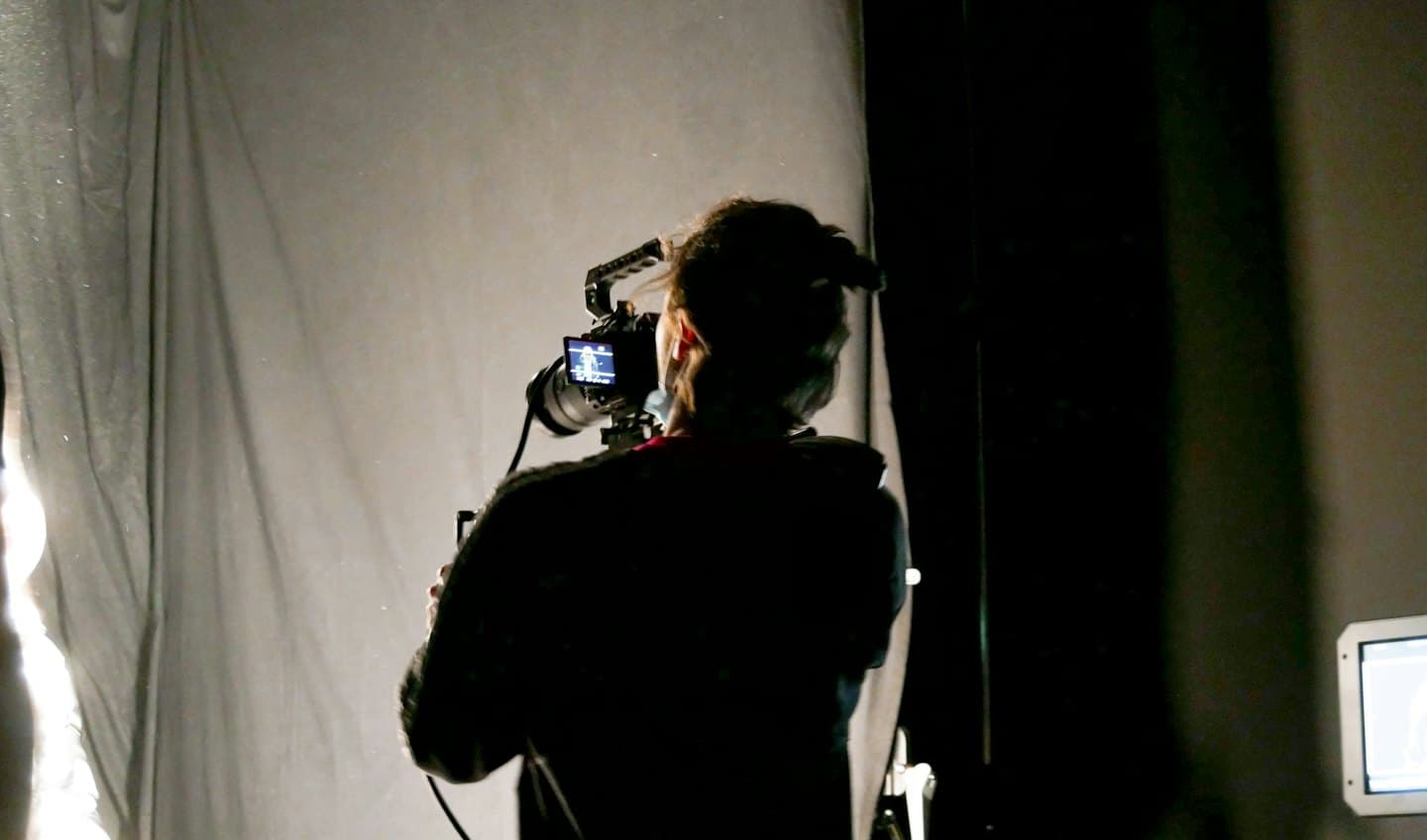 Videographer stands in a studio operating a professional camera.