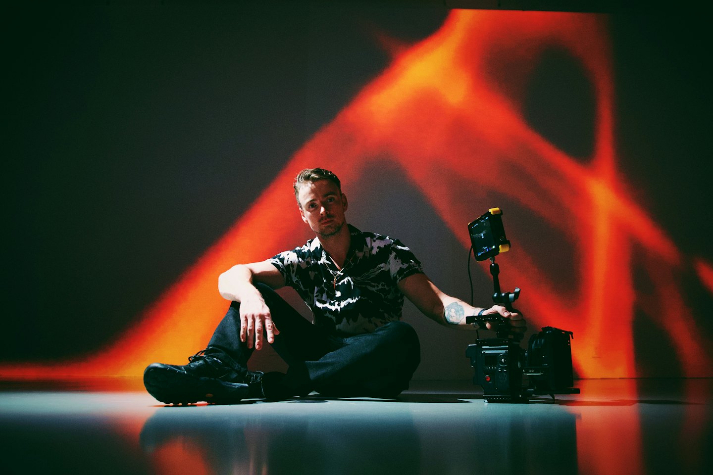 Videographer sits on a reflective floor holding a camera rig.